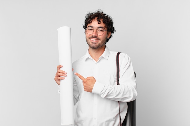 Arquiteto sorrindo alegremente, sentindo-se feliz e apontando para o lado e para cima, mostrando o objeto no espaço da cópia