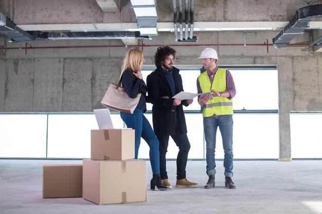 Arquiteto usando computador tablet enquanto mostra planos de design de casa para um jovem casal no canteiro de obras