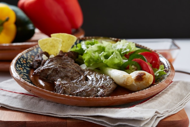 Foto arrachera con frijoles refritos cebollinas y ensalada servido en plato de barro