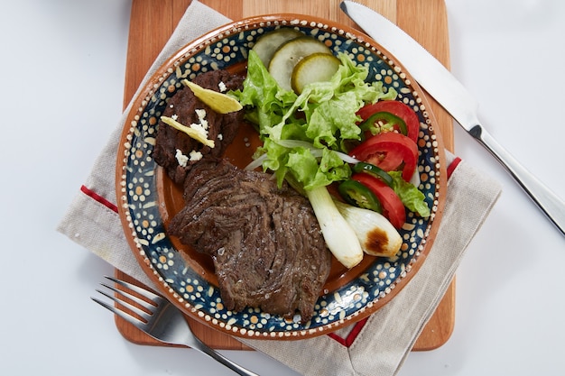 Arrachera con frijoles refritos cebollinas y ensalada servido en plato de barro