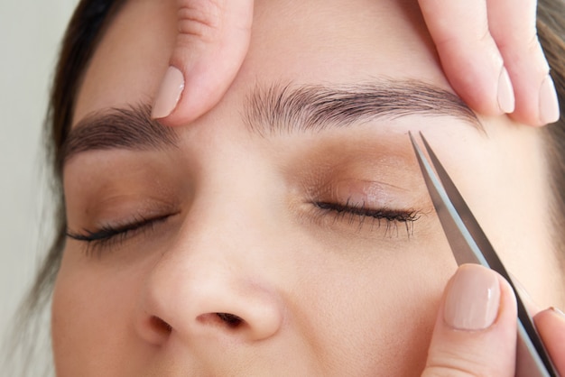 Arrancar sobrancelhas femininas com uma pinça durante a correção de sobrancelhas no salão de beleza