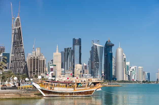 Arranha-céus no centro da cidade com primeiro plano de água e barco de Doha, Qatar.