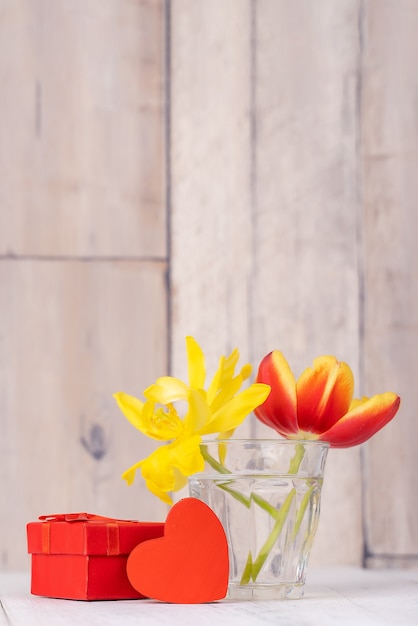 Arranjo de flores de tulipa em vaso de vidro com saudação de coração, decoração de regador na parede de fundo de mesa de madeira, close-up, conceito de design do dia das mães.