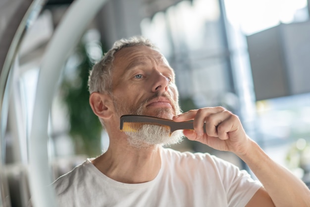 Arreglar el estilo de la barba. Un hombre peinando su barba con un peine.