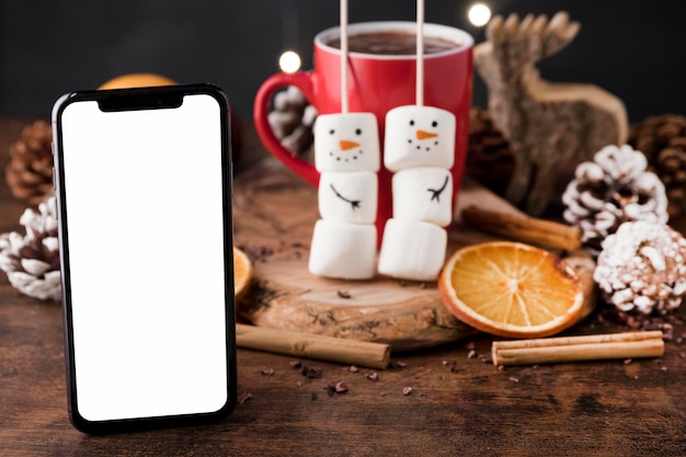 Foto arreglo de una deliciosa taza navideña de chocolate caliente y un teléfono inteligente vacío
