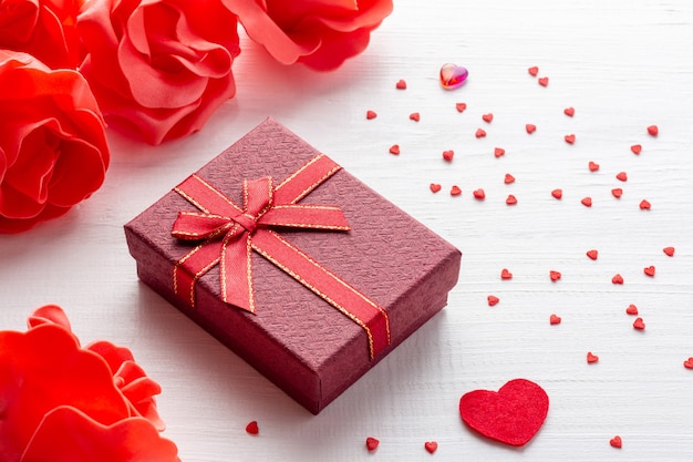 Arreglo del día de San Valentín con caja de regalo roja y corazones con flores sobre fondo blanco de madera