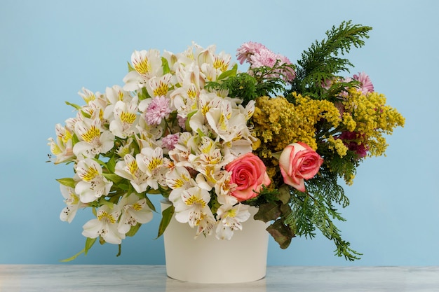 Arreglo floral con diferentes tipos de flores sobre una mesa y un fondo azul.