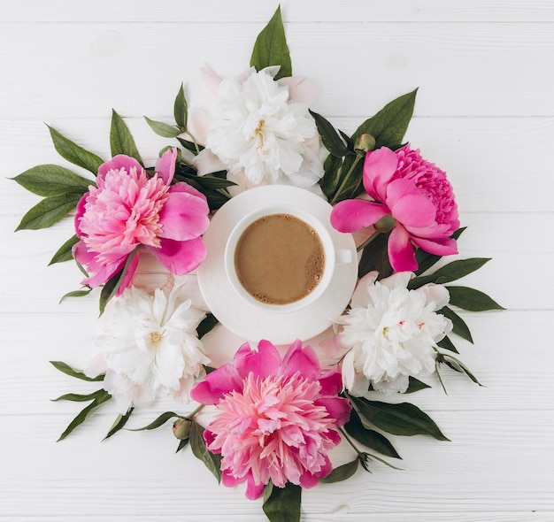 Arreglo floral de peonías rosas y blancas alrededor de una taza de café vista superior plana