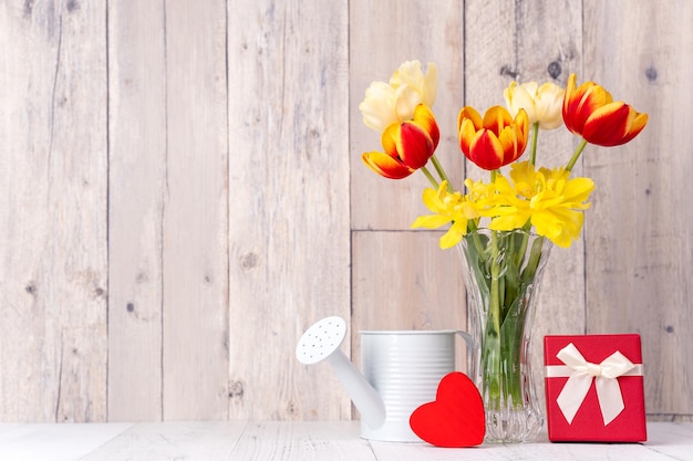 Foto arreglo de flores de tulipán en jarrón de vidrio con saludo de corazón riego puede decorar la pared de fondo de la mesa de madera de cerca el concepto de diseño del día de la madre