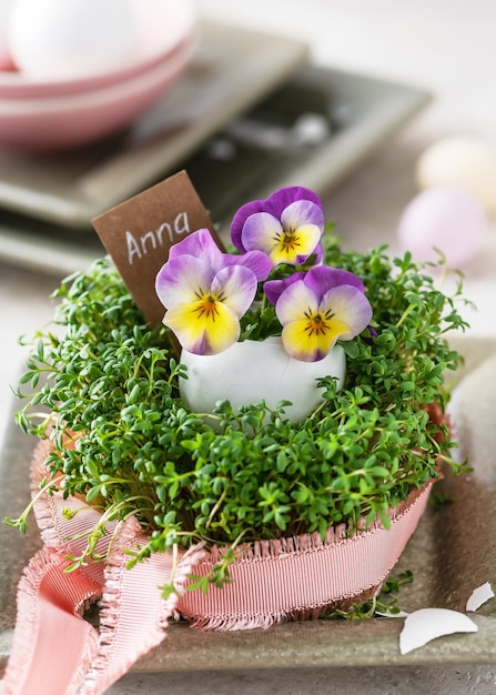 Arreglo florístico con flores violetas y amarillas de viola en jarrón de huevo y berro verde fresco