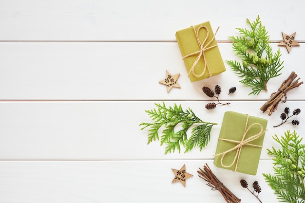 Arreglo de Navidad o Año Nuevo. Borde de cajas de regalo, ramas de coníferas y decoraciones naturales sobre fondo blanco de madera. Endecha plana, vista superior, espacio de copia.