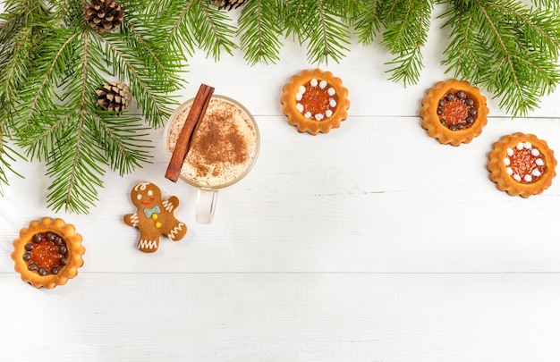 Arreglo plano de Navidad con postres navideños taza de ponche de huevo con canela, jengibre y galletas de jengibre sobre fondo de madera blanca con ramas de abeto verde, conos. Vista desde arriba. Copie el espacio.