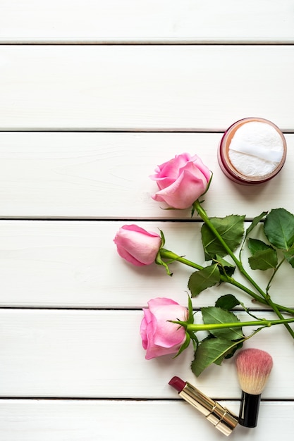 Arreglo de vista superior con maquillaje, rosas y espacio de copia sobre fondo blanco de madera