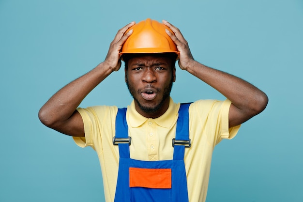 Arrependimento agarrou a cabeça jovem construtor americano africano de uniforme isolado em fundo azul