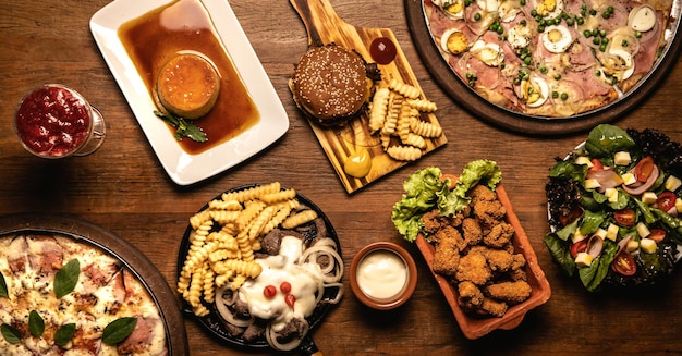 Arriba hacia abajo de comidas sabrosas en una tabla de cortar de madera con pizza, pollo frito, hamburguesa y bistec