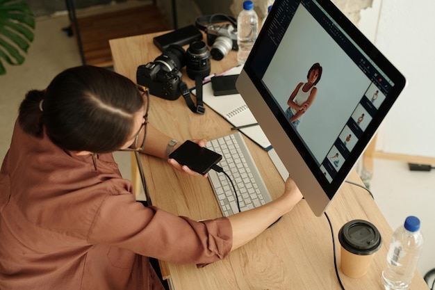 Foto arriba del ángulo de un joven fotógrafo independiente sentado frente a la pantalla de la computadora