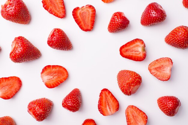 Arriba arriba foto de vista aérea de fresas enteras y cortadas haciendo un círculo aislado sobre fondo blanco.