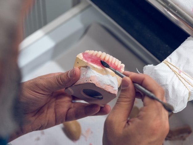 Desde arriba del cultivo, un dentista masculino irreconocible usando una espátula de acero inoxidable mientras hace implantes para prótesis de mandíbula