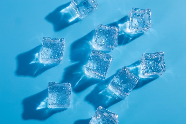 Arriba por encima de la cabeza cerrar macro vista foto de cubitos de hielo y gotas de agua sobre fondo azul.