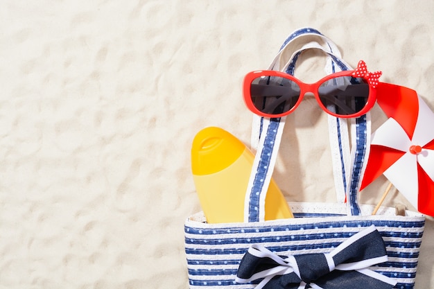 Foto desde arriba la foto de la bolsa con loción, gafas de sol y coloridos molinetes sobre arena.