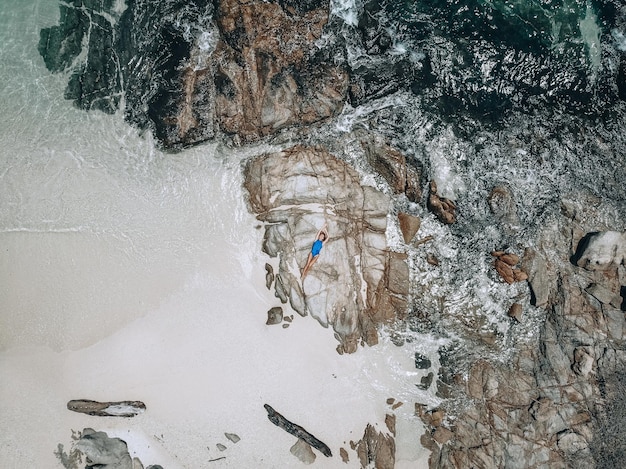 Desde arriba, la foto de una mujer joven y bonita en un traje de baño azul tumbado sobre la roca durante la marea alta. Concepto de vacaciones de verano