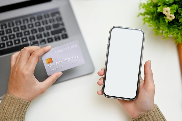 Arriba Manos femeninas sosteniendo su teléfono inteligente y tarjeta de crédito sobre su moderno escritorio de trabajo