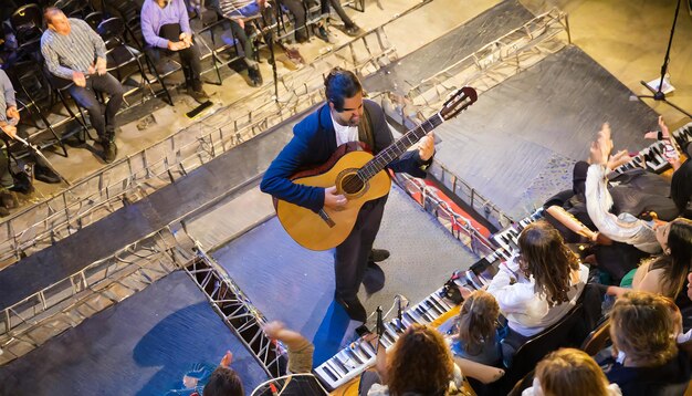 Desde arriba un músico masculino en el escenario tocando una guitarra con pasión rodeado de una audiencia inmersa...