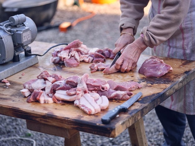 Desde arriba de una persona irreconocible cortando carne cruda con un cuchillo afilado sobre una mesa de madera mientras preparaba un manjar tradicional español en Matanza en Mallorca