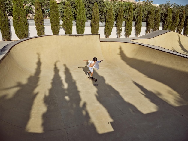 Desde arriba, toda la longitud del niño montando longboard en rampa en el parque de patinaje en un día soleado