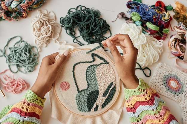 Arriba se ven las manos de una joven diseñadora haciendo un bordado creativo