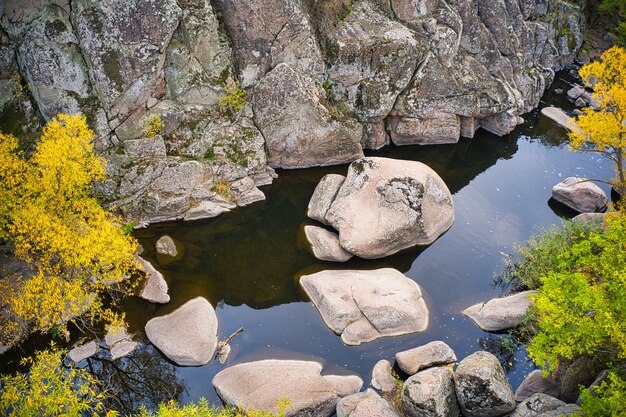 Un arroyo fluye en el Cañón Aktovsky, Ucrania. Árboles otoñales y grandes cantos rodados de piedra alrededor. Disparo de drone panorámico aéreo