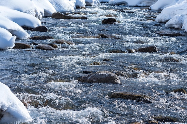 Arroyo de primavera en un río de montaña entre el fondo del paisaje de los bancos nevados