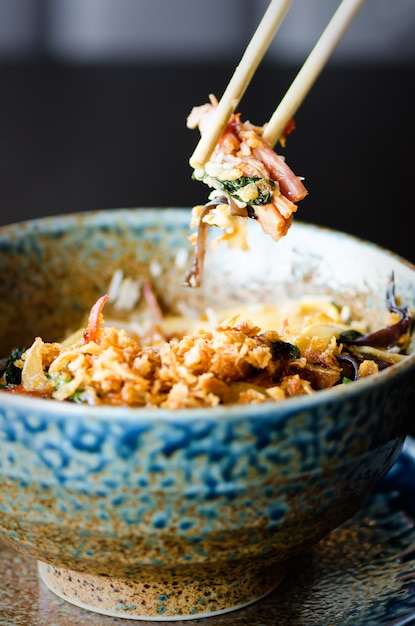 Foto arroz asiático con cerdo, champiñones mu-err, col napa, brotes de bambú en escabeche, espinacas, teriyaki, salsa de chile dulce, chips de cebolla en un tazón de cerámica.