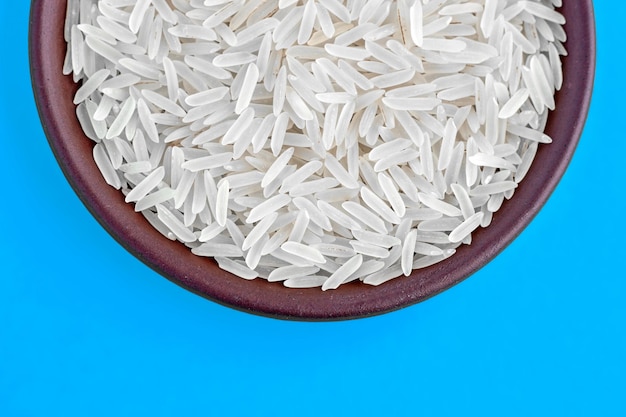 Arroz basmati blanco sin gluten en un cuenco de arcilla marrón aislado sobre un fondo azul Vista superior con espacio para copiar