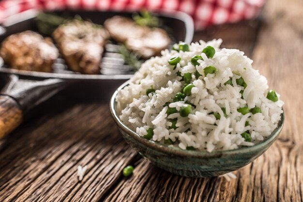 Arroz basmati com ervilhas em uma tigela e peito de frango grelhado no fundo.