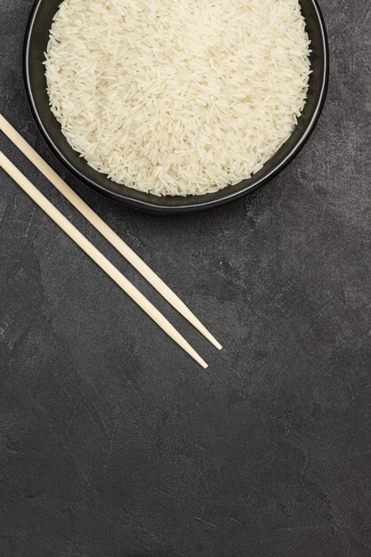 Arroz basmati en cuenco negro. Palos de bambú en la mesa.