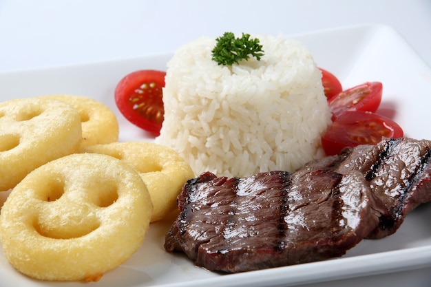 arroz, bife e batatas fritas no prato.