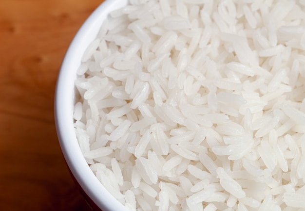 arroz blanco cocido en un tazón blanco sobre una tabla de cortar de madera vista superior