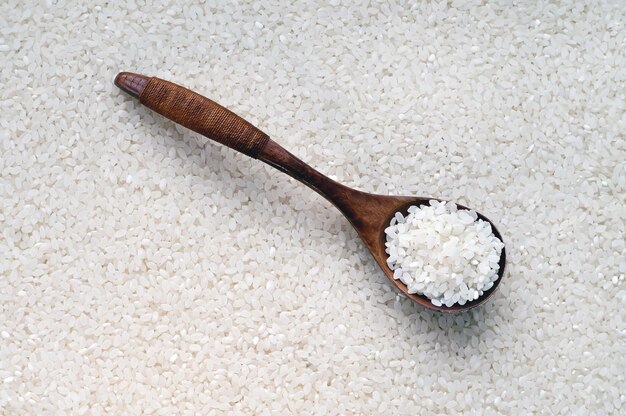 Arroz blanco crudo en una cuchara de madera Fondo de enfoque selectivo de arroz blanco redondo en el avión