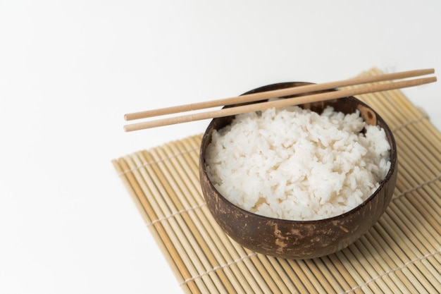 Arroz blanco en un tazón de coco sobre un fondo blanco. Foto minimalista con arroz y palillos de bambú.