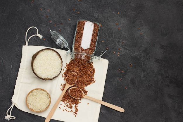 Arroz branco com casca de coco arroz vermelho em frasco de vidro colheres de madeira com arroz vermelho saco de embalagem de linho copiar espaço plano lay fundo preto