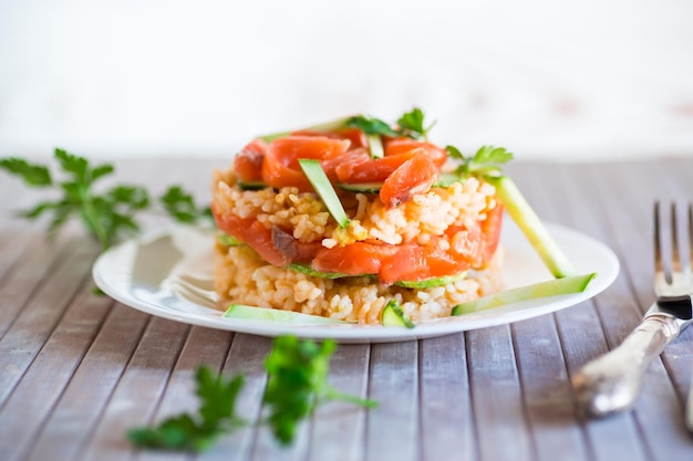 Arroz branco cozido com pepinos de peixe vermelho salgado e outros vegetais com ervas num prato sobre uma mesa de madeira