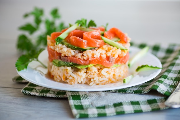 Arroz branco cozido com pepinos de peixe vermelho salgado e outros vegetais com ervas num prato sobre uma mesa de madeira