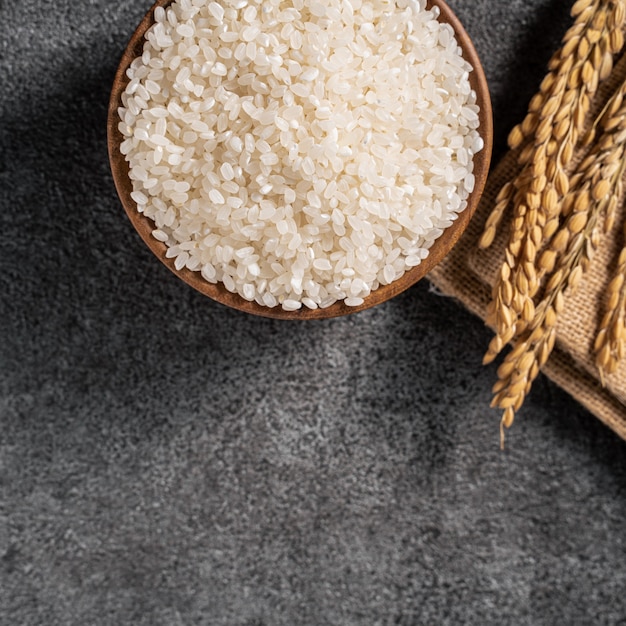 Arroz branco cru em uma tigela com a orelha no fundo preto escuro da mesa.