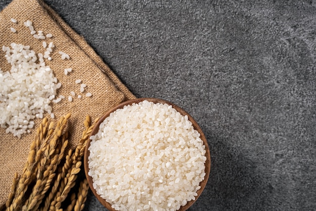 Arroz branco cru em uma tigela com a orelha no fundo preto escuro da mesa.