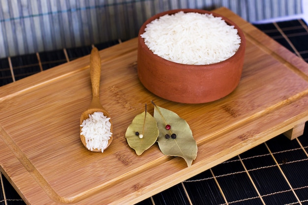 Arroz branco em uma tigela de barro e em uma colher de pau. folhas de louro e