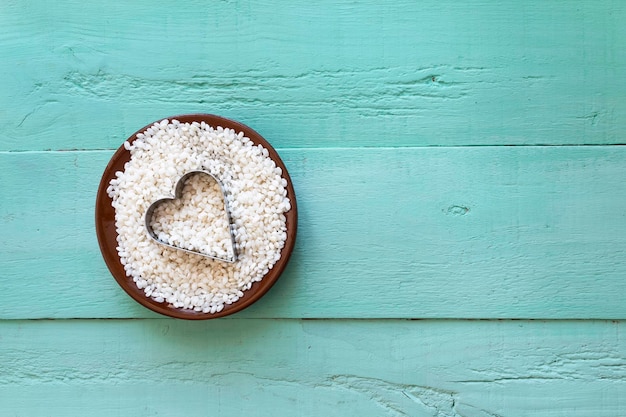 Arroz branco redondo cru em uma tigela de barro em um fundo de madeira turquesa