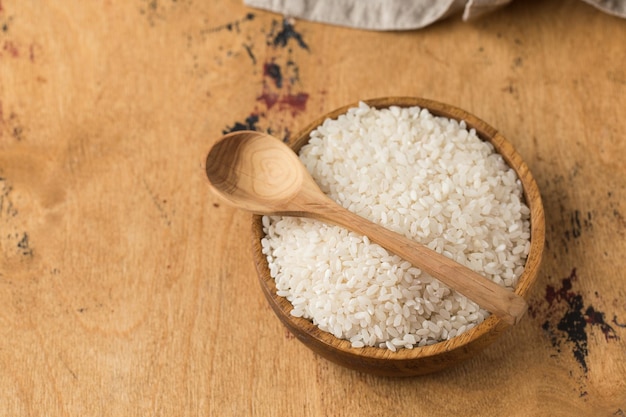 Arroz branco redondo cru em uma tigela de madeira e em uma colher de madeira sobre um fundo de madeira