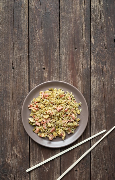 Arroz cantonês ou arroz frito chinês em um prato e pauzinhos de madeira em uma mesa velha de madeira escura