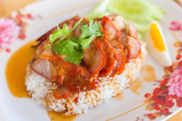 Arroz con cerdo rojo asado cerdo crujiente y huevo cocido cubierto con salsa en un plato blanco